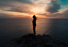 Woman Enjoying Relaxing Moment On Cliff At Sunset