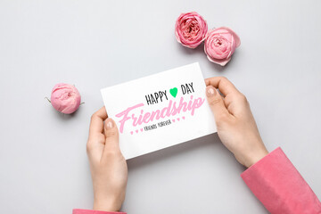 Wall Mural - Female hands holding paper with text HAPPY FRIENDSHIP DAY and flowers on light background