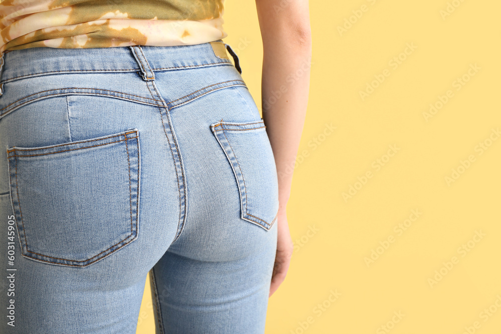 Young woman in stylish jeans on yellow background, back view