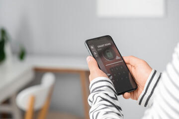 Young man with mobile phone using smart home security system application in bedroom, closeup