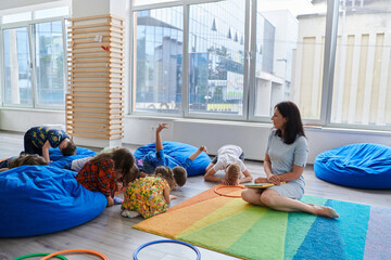 Wall Mural - Reading time in an elementary school or kindergarten, a teacher reads a book to children in an elementary school or kindergarten. The concept of pre-school education. Selective focus