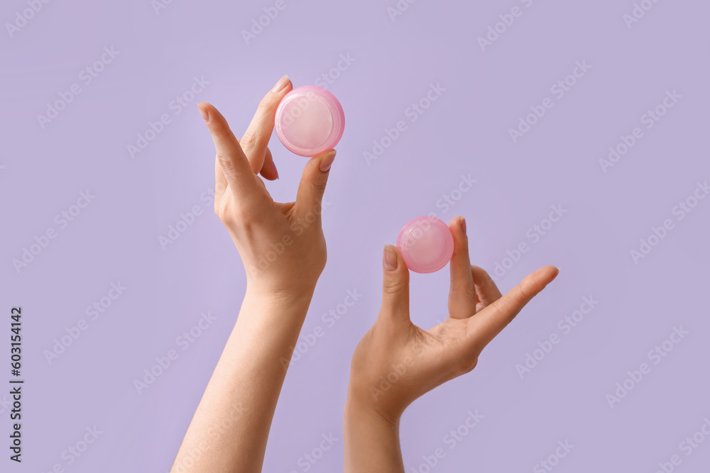 Hands holding jars of cream on lilac background