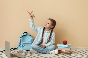 Poster - Little girl with wooden airplane sitting near beige wall. Children's Day celebration