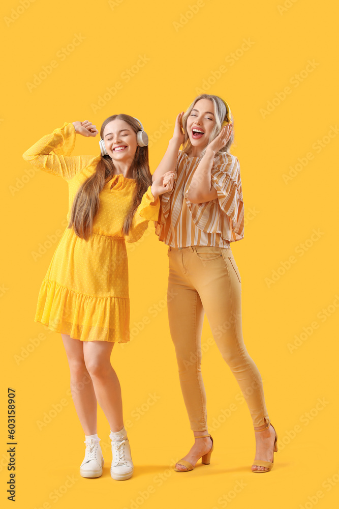 Young sisters in headphones on yellow background
