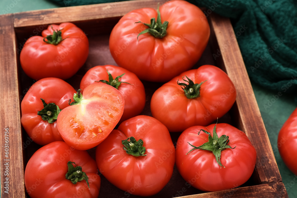 Wooden box with fresh tomatoes on green background