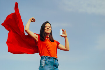 Strong Superhero Girl Holding a Bottle of Pills Feeling Strong. Happy woman flexing her muscles taking supplements 

