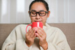 © Pornpimon - Portrait of a young woman enjoying a cup of coffee at home. Beautiful woman in white sweater smiling drinking hot coffee in the morning. Lifestyle, free time and relaxation.