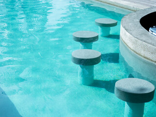 Empty round terrazzo bar stools seat in clean and clear water swimming pool preparing for the guests at the resort on sunny day. Pool bar exterior on summer background.