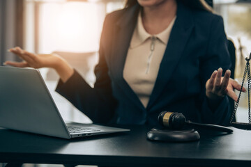 Beautiful young woman lawyer sitting in front of laptop in room with documents and smartphone with empty hammer and scale next to it justice and legal concept