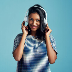 Poster - Woman, portrait and headphones with music in studio with happiness and web audio. Blue background, Indian female person and young model listening, hearing and streaming a song with smile and online