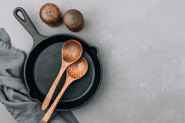 Wall Mural - Empty pan. Cast iron pan with wooden spoons on gray stone background, top view, copy space.