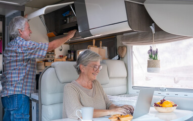 Happy retired caucasian couple enjoying freedom and alternative lifestyle traveling in camper van. Senior woman browsing on laptop on a leisure trip enjoying travel vacation retirement