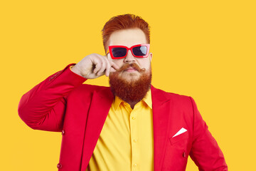 Fashionable cool redhead man in suit and sunglasses isolated on yellow studio background. Trendy red-haired male with mustache in eccentric wear and spectacles pose. Fashion and style.