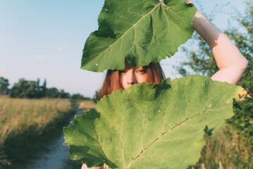 woman looks out from behind two large green leaves. Emphasis on the eyes.	