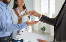 Realtor Or Real Estate Agent With A Clipboard Hands Over The Key To A Young Couple. Happy Family Buys A New House Or Apartment And Takes The Key From The Realtor. Buying House Concept