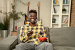 © JustLife - Young man watching tv at home. African sitting on the sofa, enjoy at home.