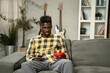 © JustLife - Young man watching tv at home. African sitting on the sofa, enjoy at home.