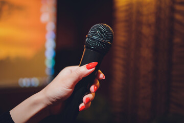 Wall Mural - Microphone and female singer close up. Woman singing into a microphone, holding mic with hands.