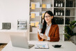 © Nuttapong punna - Confident beautiful Asian businesswoman typing laptop computer and digital tablet while holding coffee at office
