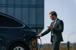 © standret - Holding the charger. Businessman is standing near his electric car outdoors