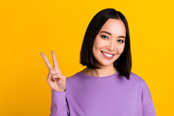 Poster - Photo of shiny charming woman wear violet shirt showing v-sign smiling empty space isolated yellow color background