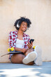 © Alvaro - young afro girl smiling listening to music on her smartphone with her skateboard resting on her legs