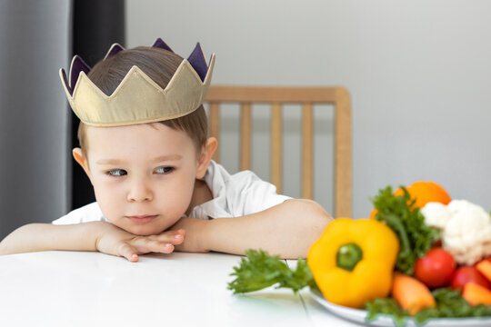 Wall Mural - portrait of a boy at the table next to fresh vegetables, problems with teaching a child healthy fresh food