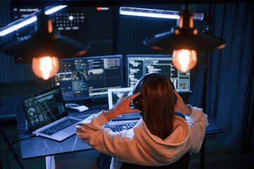 looking at screens. young professional female hacker is indoors by computer with lot of information 