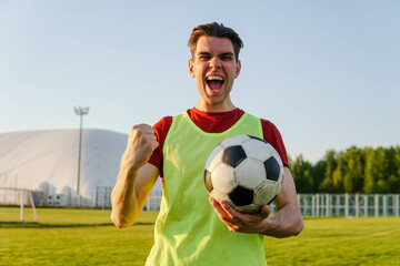 Happy male football player in sportwear celebrating victory, holding soccer ball