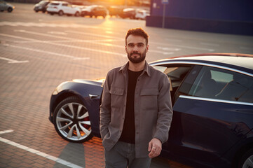 Wall Mural - Sunny background. Man is standing near his electric car outdoors