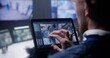 © Framestock - Close up shot of security officer zooming CCTV cameras with AI facial scanning using tablet in police surveillance center. Colleagues work at background. Monitoring system. Concept of social safety.