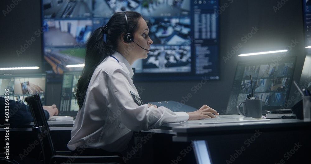 Female operator in headset types keyboard and controls security cameras ...