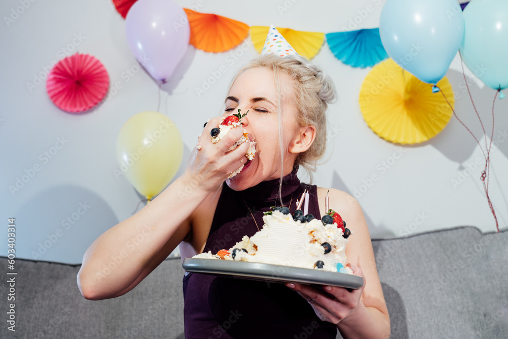 Woman in festive dress and party cap eating birthday cake with her ...