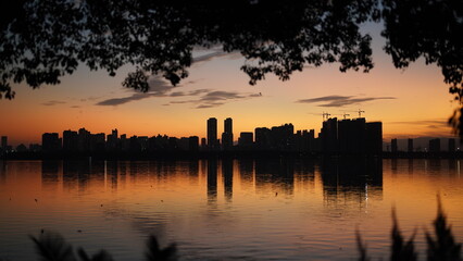 Wall Mural - the beautiful sunset view with the buildings' silhouette and orange color sky mirrored in the peacef