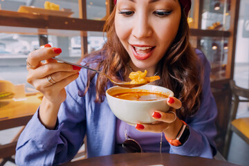 Wall Mural - Happy girl eating spicy thai soup Tom Yam in authentic restaurant