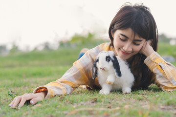 Wall Mural - White rabbit survey on green grass floor with owner eye of love and care , beautiful and cute moment with woman and animal.