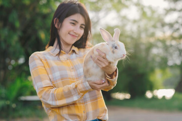 Wall Mural - Backlit of cute bround white and pink ear rabbit in woman hand with blur woman and green forest bavkground.