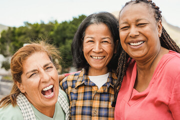 Wall Mural - Happy multiracial elderly friends smiling in front of camera - Senior women hugging each other outdoor