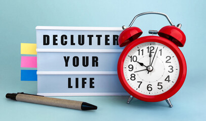 Poster - text declutter your life written on the lightbox with alarm clock and colorfull stickers on blue bac