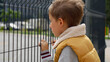 Portrait of upset little boy feeling alone looking through metal fence. Child depression, problems with bullying, victim in school, emigration, criminal and poverty