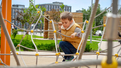 Canvas Print - Little boy climbing through obstacles of ropes and nets on new public playground. Active child, sports and development, kids playing outdoors