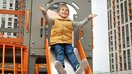 Wall Mural - Cheerful smiling boy having fun sliding down the slide at new playground. Active child, sports and development, kids playing outdoors