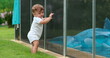 Toddler baby standing by swimming pool fence, drowning prevention, protection grid