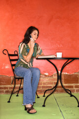 Attractive young adult woman sitting in front of a colorful wall. She is reading a book and talking on a cellphone. Vertical shot.