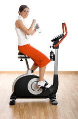 Wall Mural - Young woman training on exercise bike at the gym and drinking water