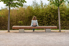 Woman Sitting On Her Back Resting On A Wooden Bench In A Park Next To The Ebro River, Zaragoza.