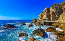 Surfer waves turquoise blue water rocks cliffs boulders Puerto Escondido.