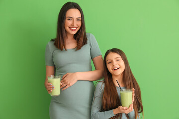 Sticker - Little girl with her pregnant mother drinking smoothie on green background