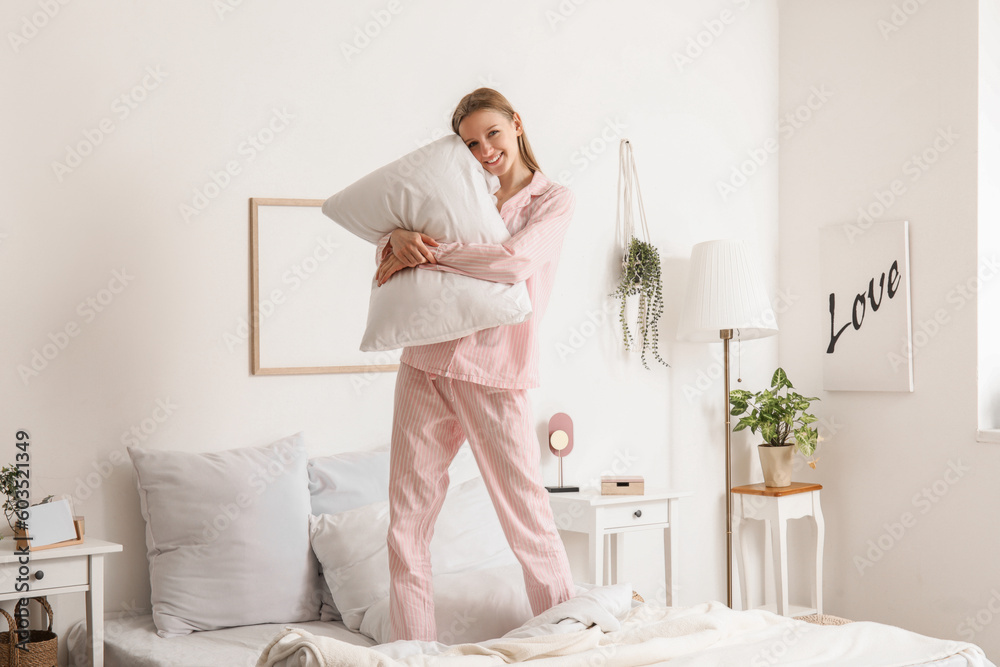 Pretty young woman with soft pillow in bedroom