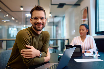 Happy entrepreneur working on computer in office and looking at camera.